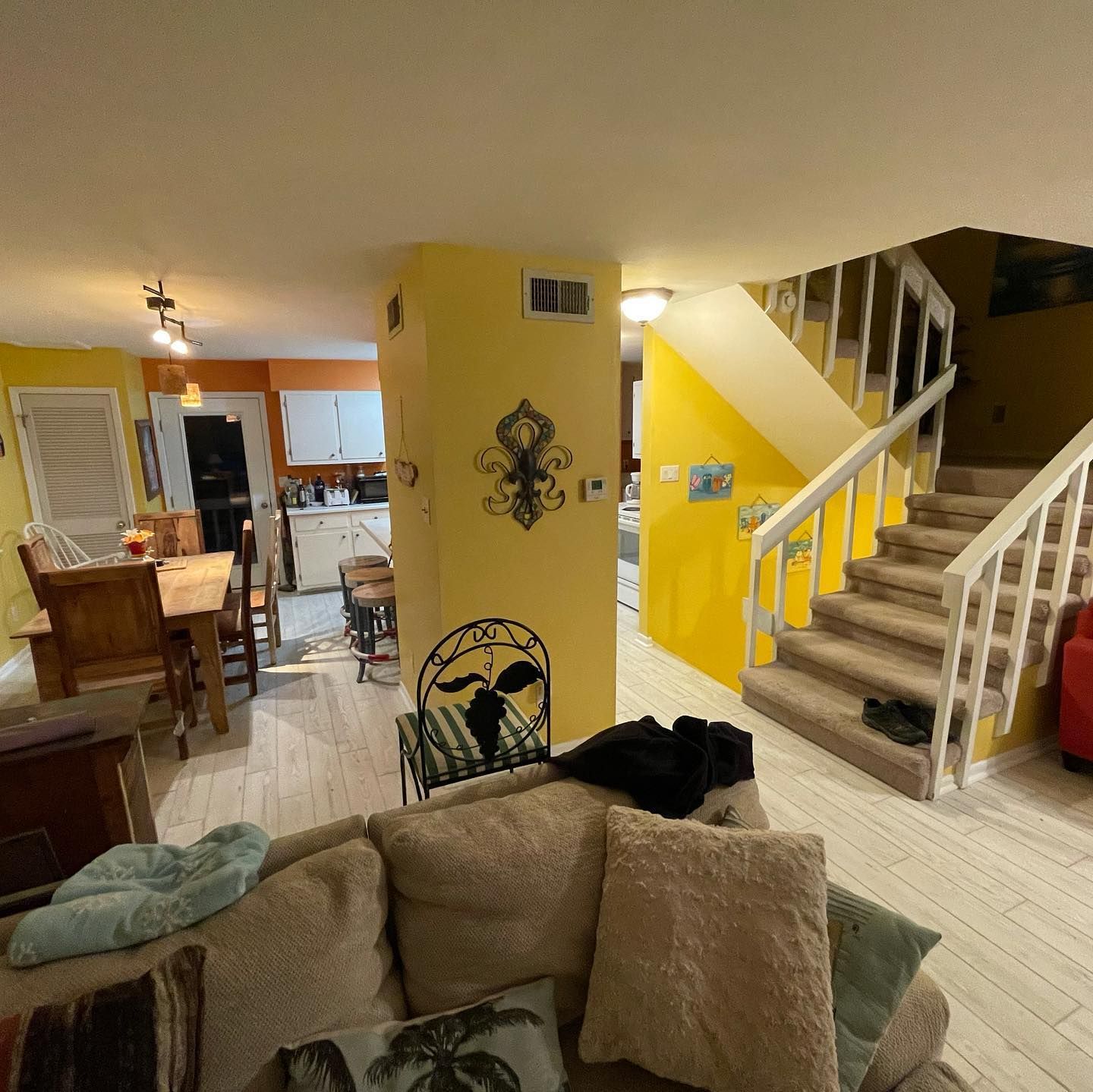 Living room with yellow walls, stairs, kitchen, and a sofa.