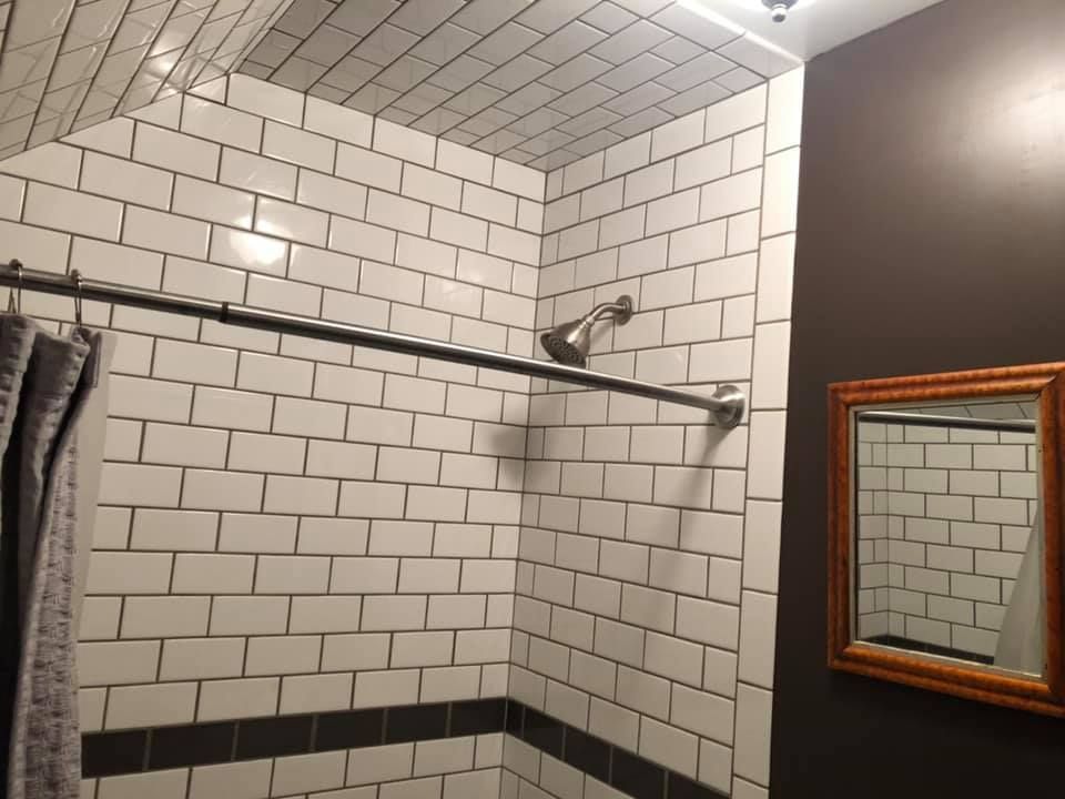 Shower stall with white subway tiles and black grout. Brown walls with a gold-framed mirror.