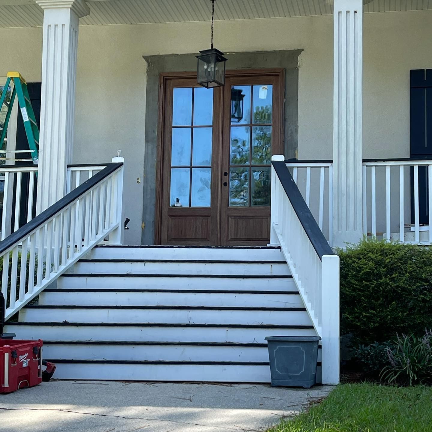 Front porch with stairs, double wooden doors, white railing, black accents, and columns.