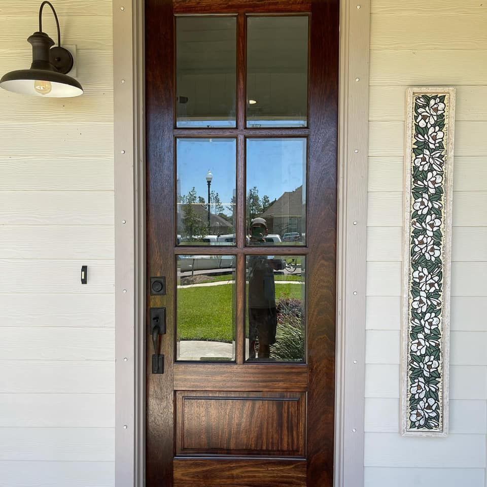 Wooden front door with glass panels, black hardware, and a matching wall sconce on a white siding house.