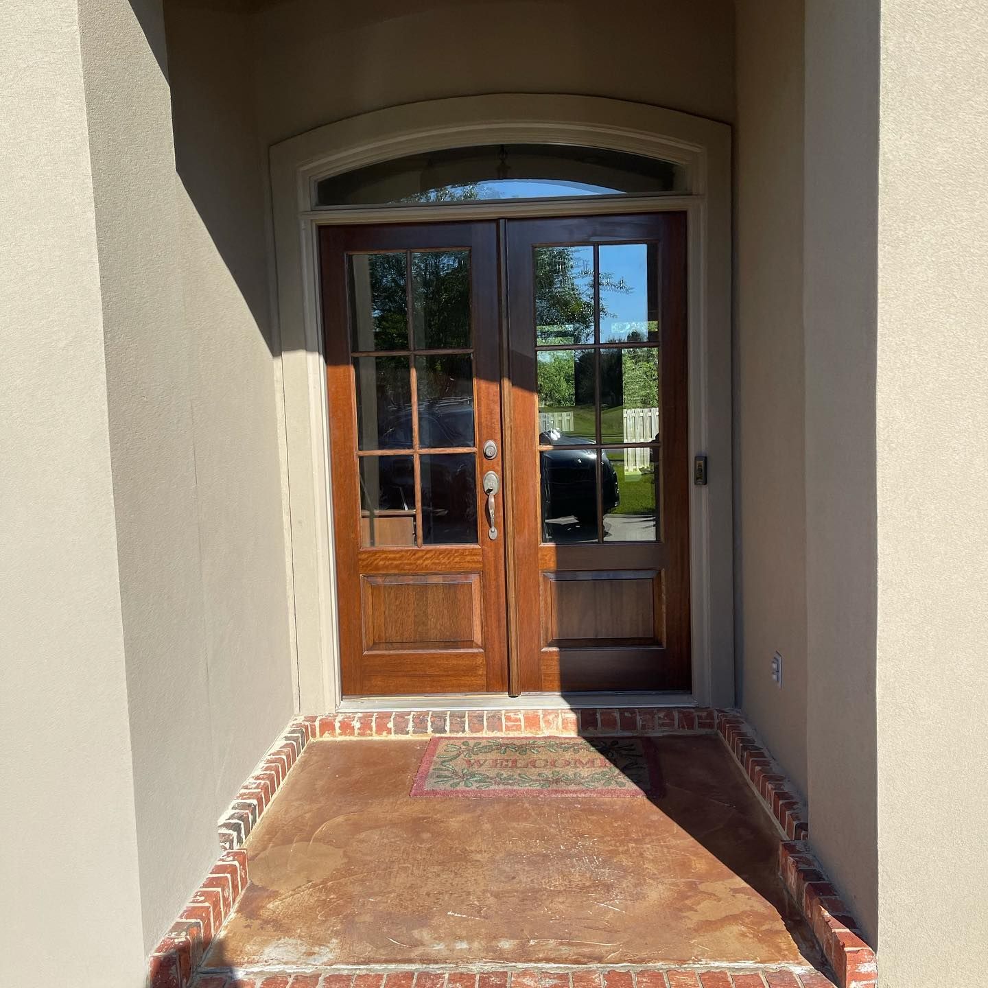 Wooden double doors with glass panes and arched window, in a tan doorway with a brick border.