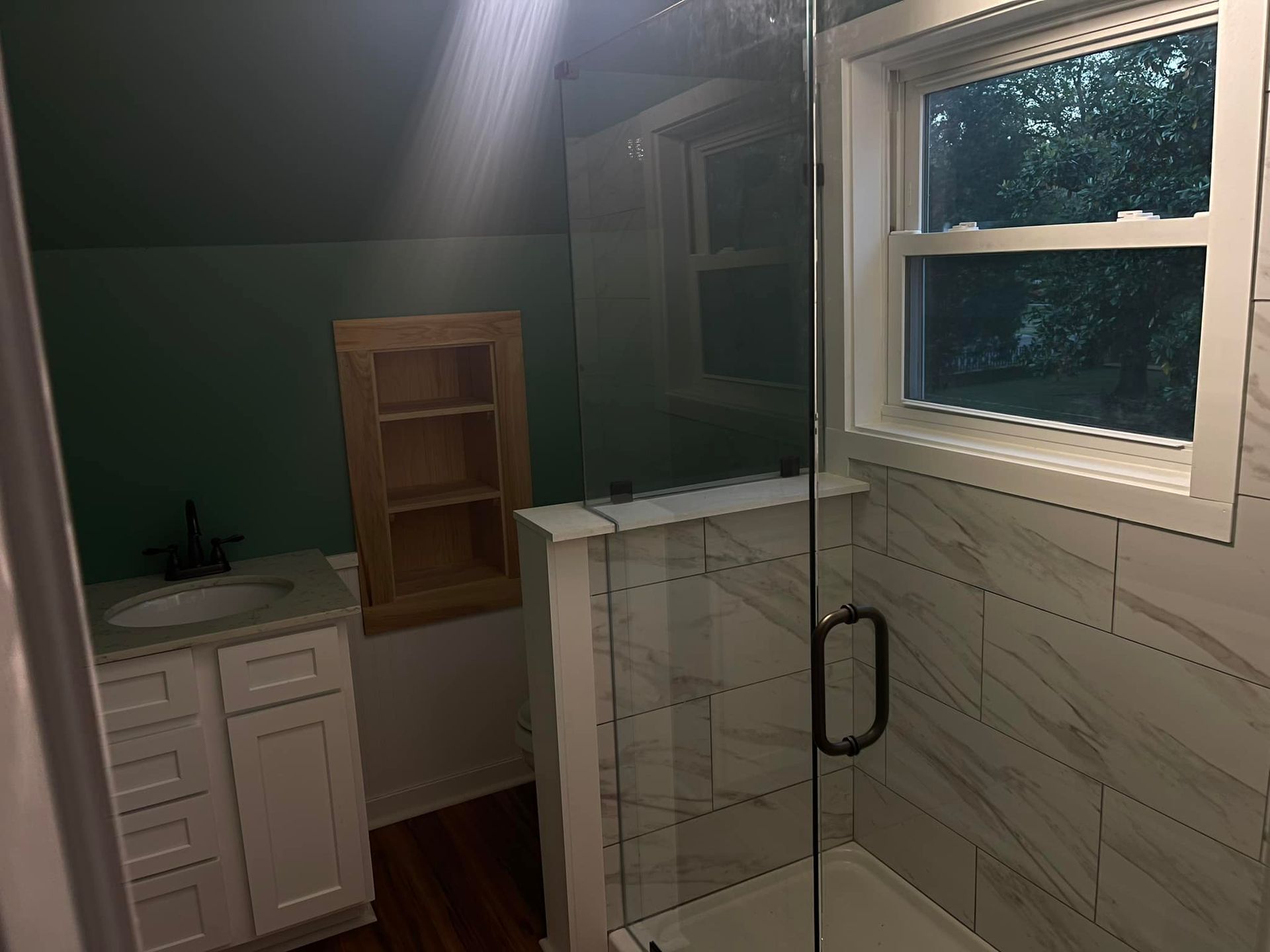 Bathroom with white vanity, shower, green wall, wood floor, and window.