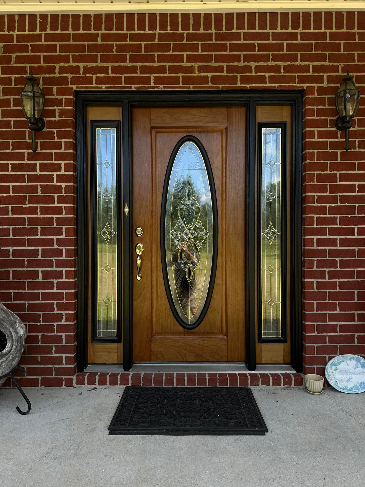 Red brick building with a wooden door, sidelights, and black trim. Two sconces flank the door.