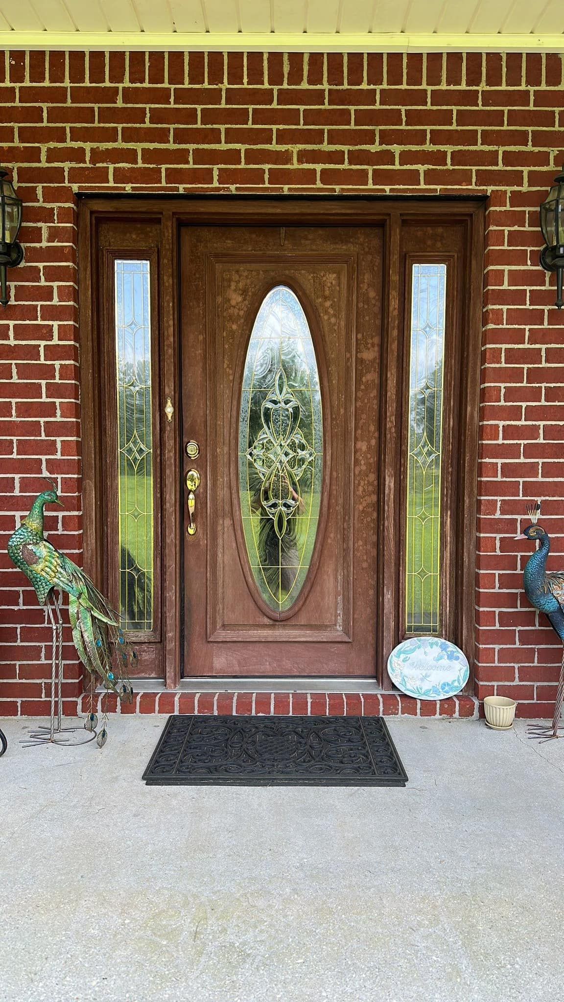 Red brick house front door with oval glass, flanked by side panels and peacock statues.