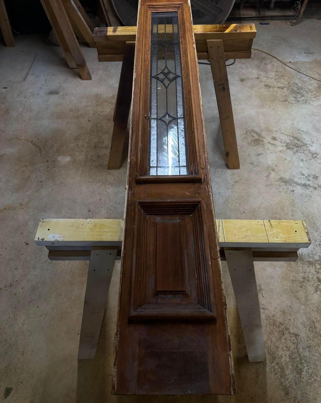 Wooden door with glass panel and decorative elements, resting on sawhorses.