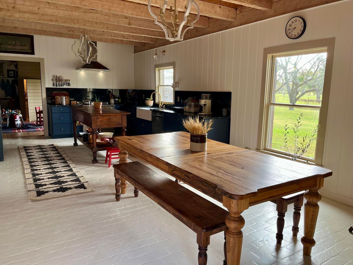 A kitchen with wood-paneled walls, a stainless steel refrigerator, white cabinets, and pots hanging on the wall.