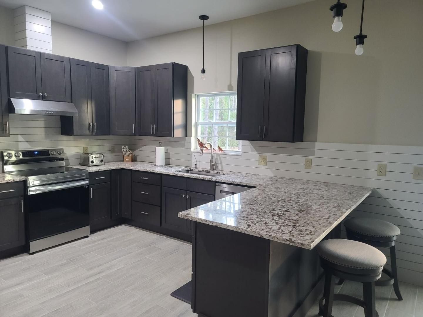 Modern kitchen with dark cabinets, stainless steel appliances, and a granite countertop island.