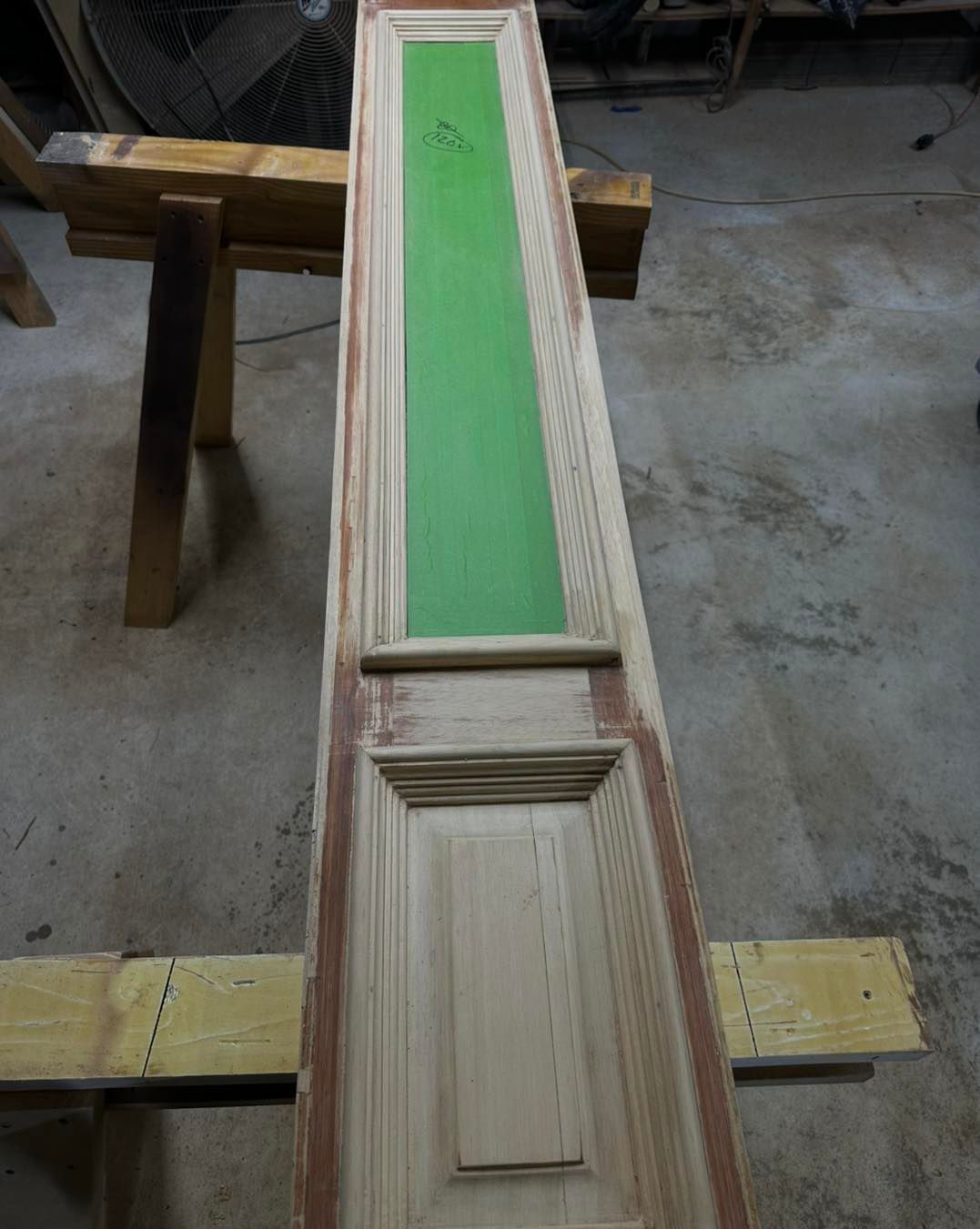 Door with a central green painted section, resting on a wooden sawhorse.