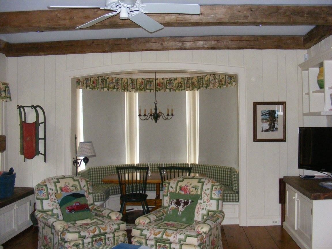Cozy living room with armchairs, a built-in dining nook, and exposed wooden beams.