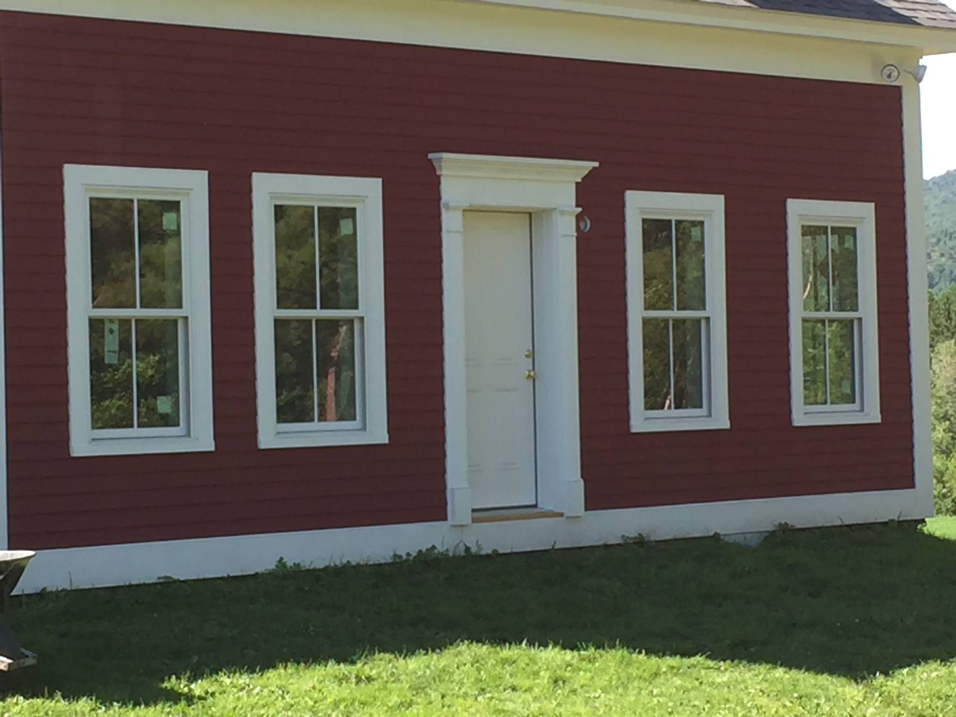 Red building with white trim, door, and windows; green grass and trees in the background.