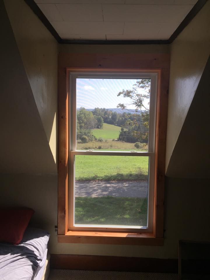Window with wooden trim, looking out on a green field and trees. Light streams in, highlighting the room's angled walls.