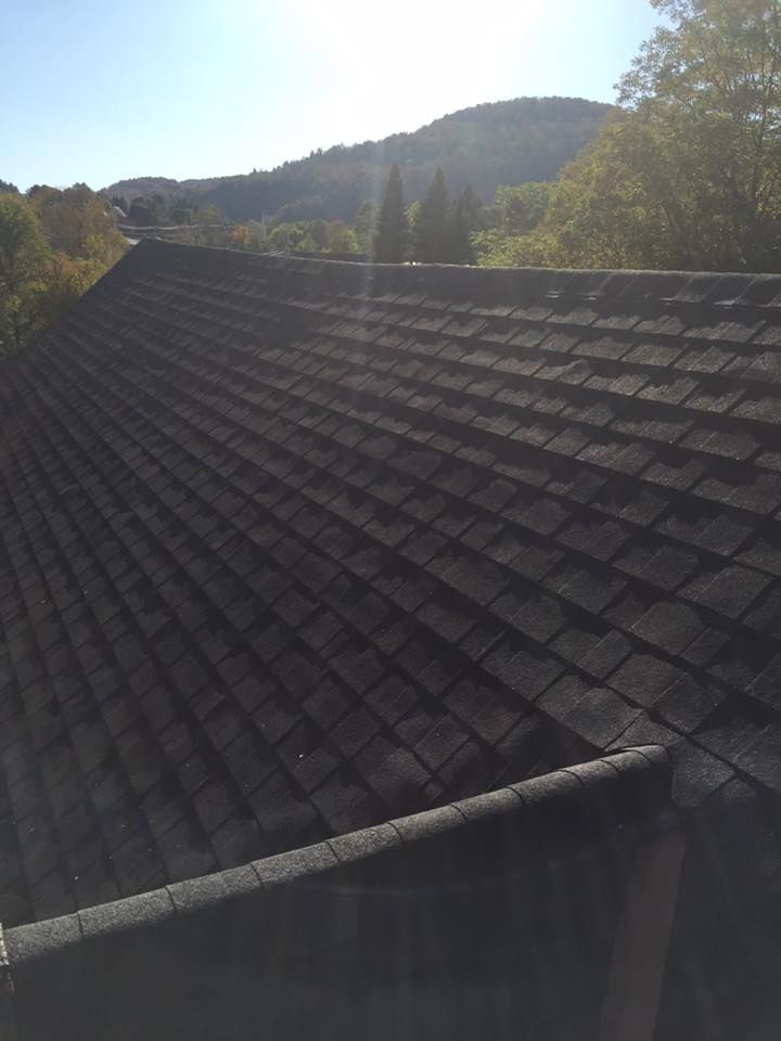 Dark shingle roof with a mountainous landscape in the background under a sunny sky.