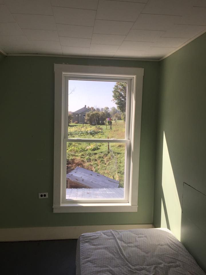 Room interior with a window overlooking a green field, a white mattress is on the floor.