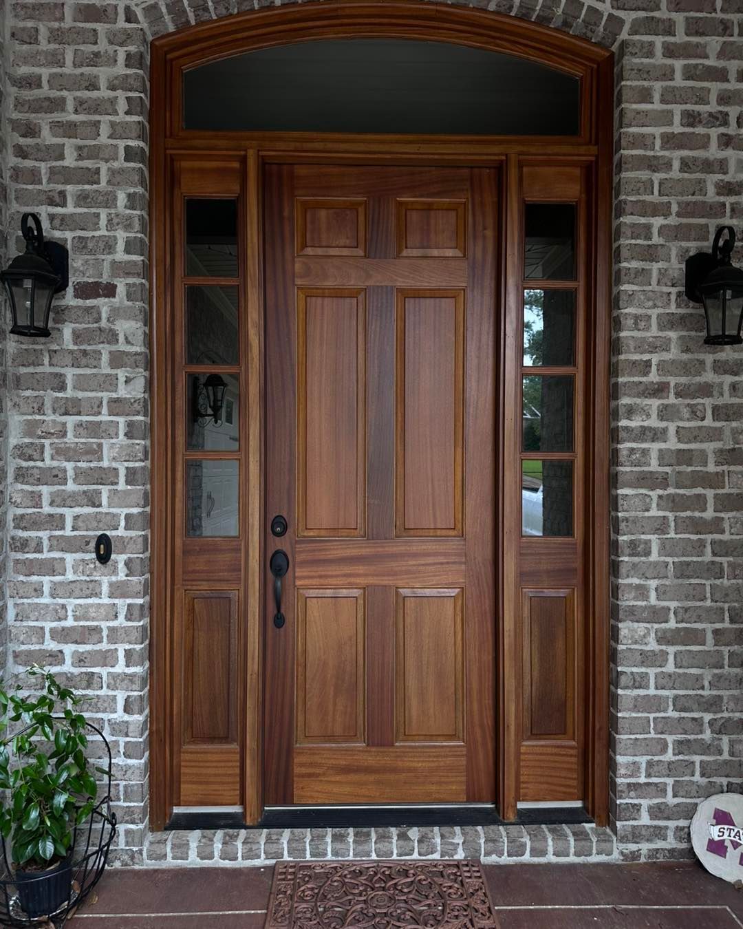 Double wooden doors with glass panels reveal a car parked outside on a sunny day; a patterned rug lies in front.