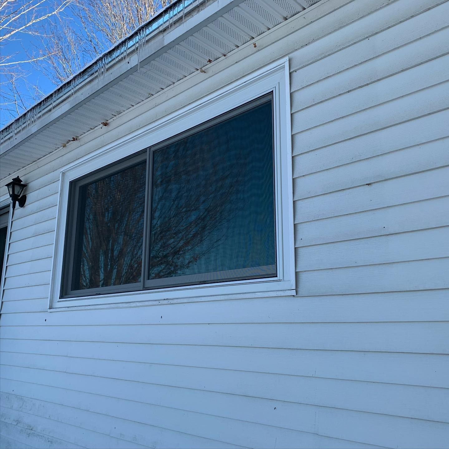 White siding on a house with a rectangular window framed in white. The window reflects trees.