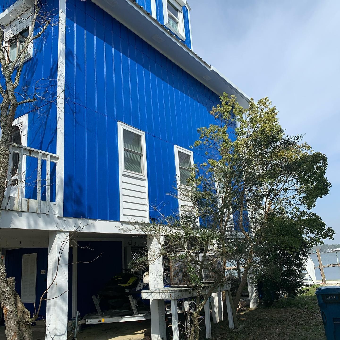 Blue two-story house on stilts with white trim and windows. Trees in front.