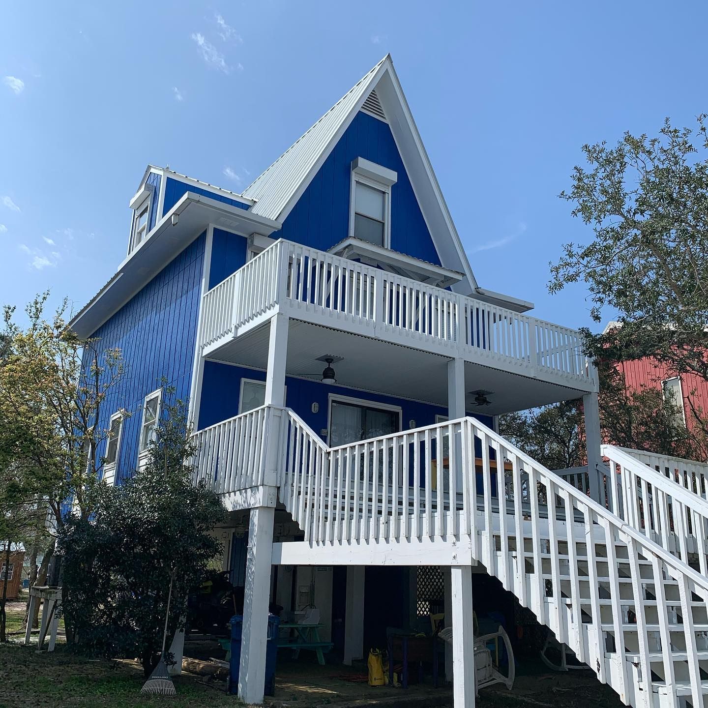 Blue and white two-story house with a large deck and stairs. Blue siding, white trim, and a bright sky.
