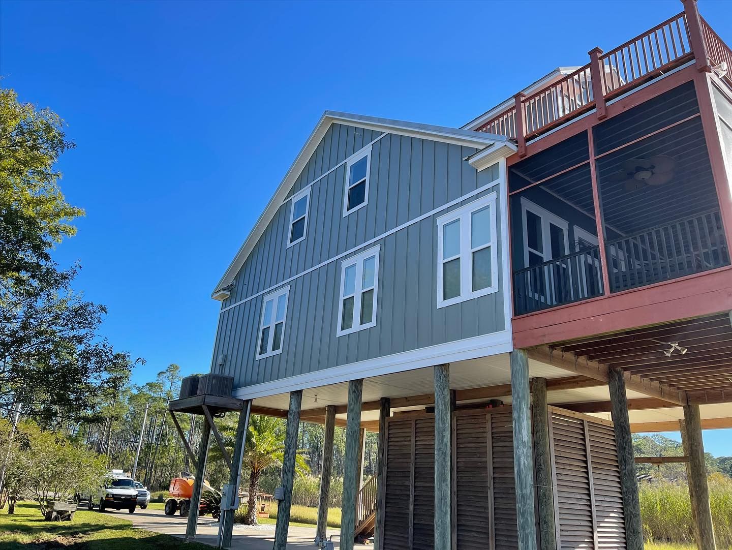 Two-story blue beach house on stilts with a screened porch and clear blue sky.