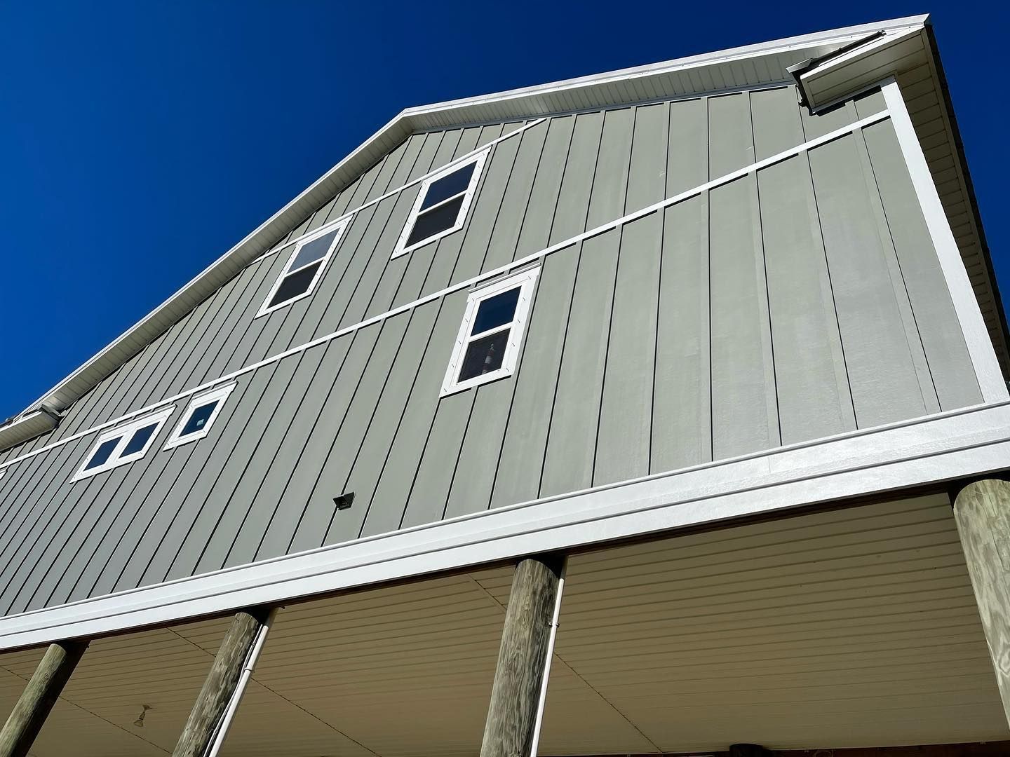 Gray house with white trim, vertical siding, raised on posts against a blue sky.
