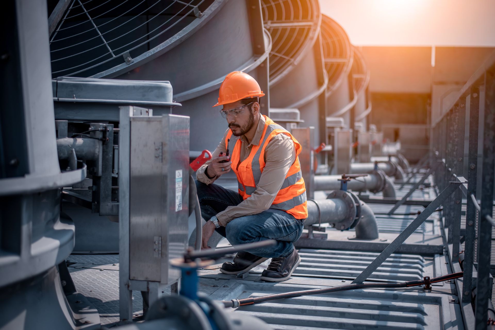A man wearing a hard hat and safety vest is working on a machine.