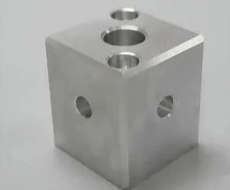 A metal cube with three holes in it is sitting on a table.