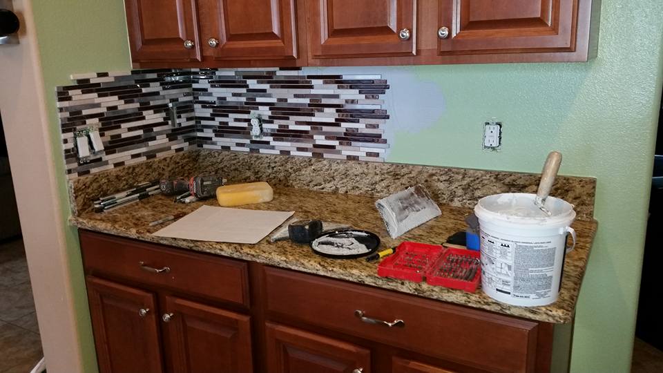 A kitchen counter with a bucket of paint and tools on it.