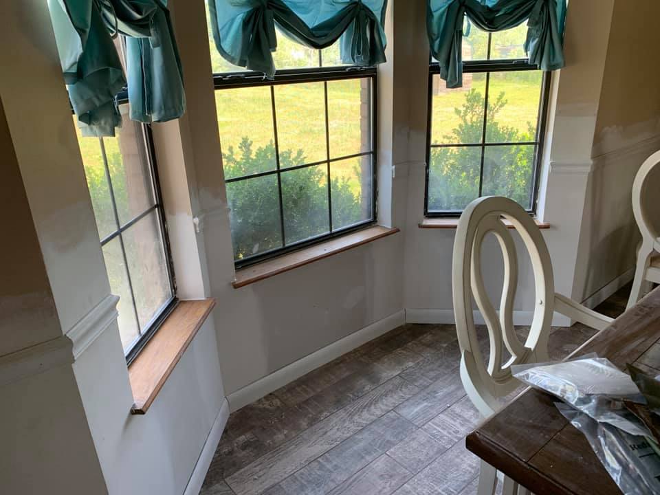 A dining room with a table and chairs and two windows.