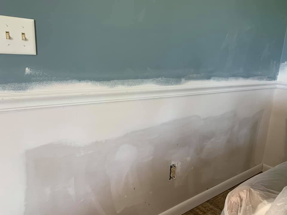 A room with a blue wall and white trim is being painted.