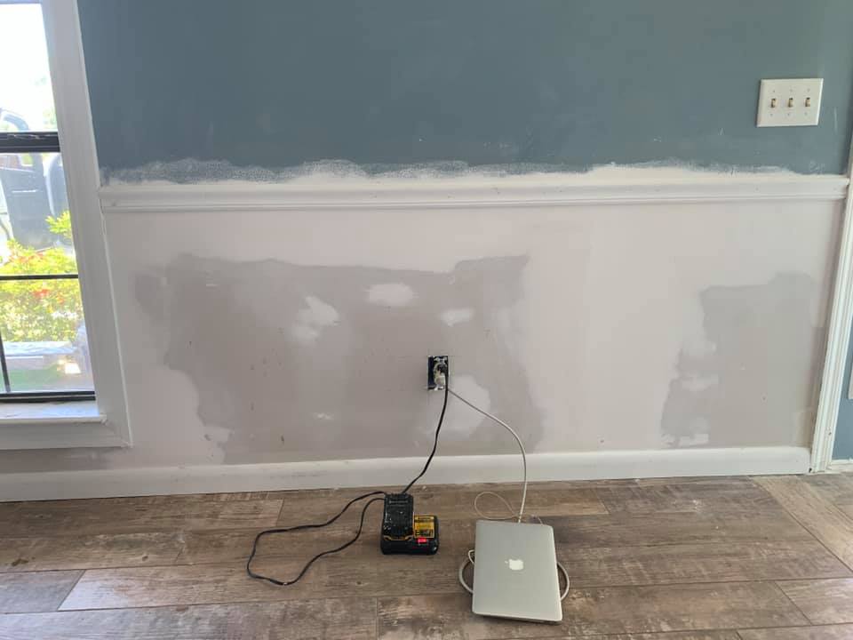 A laptop is sitting on a wooden floor next to a wall.