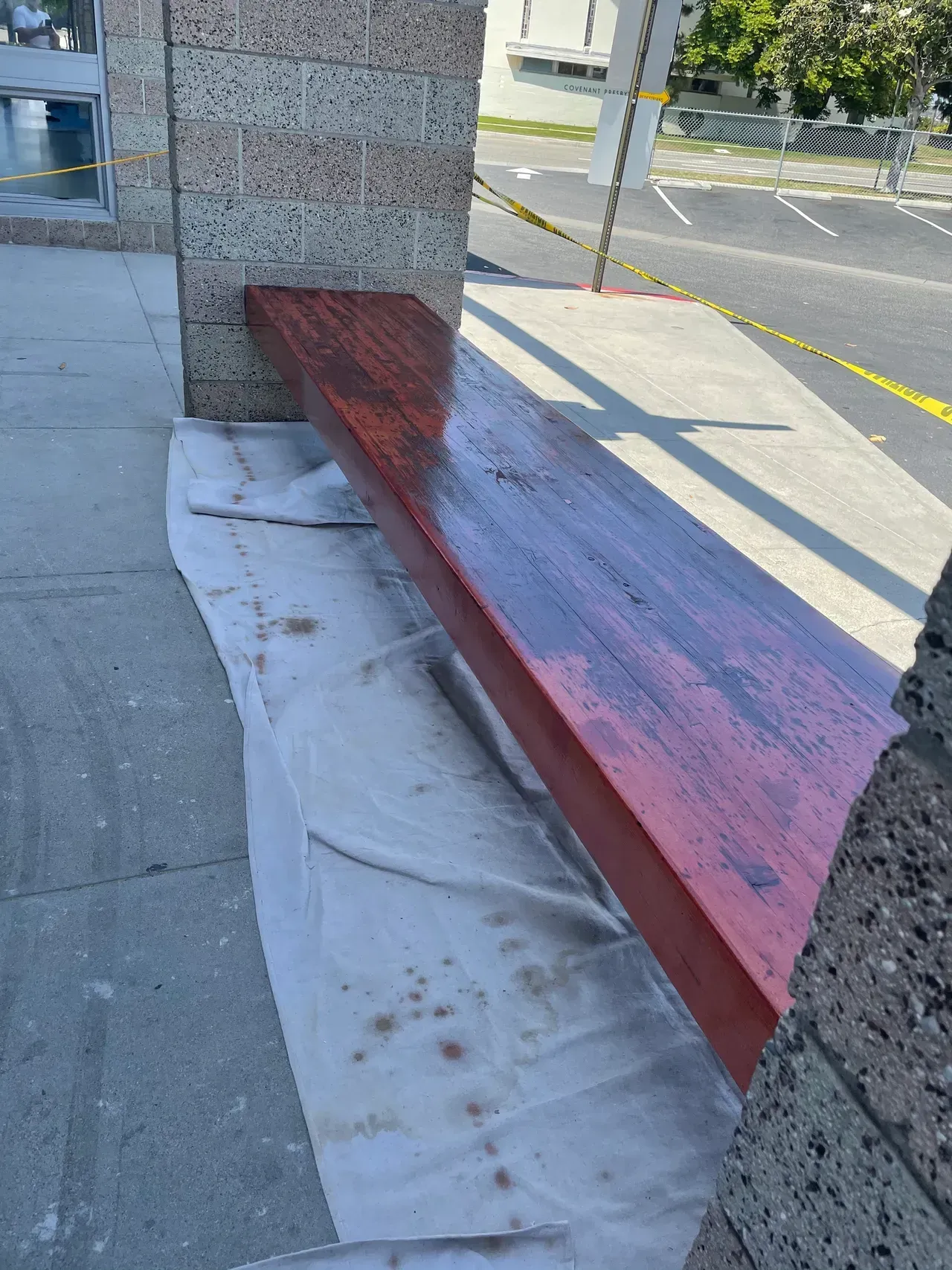 A wooden bench is being painted red on a sidewalk