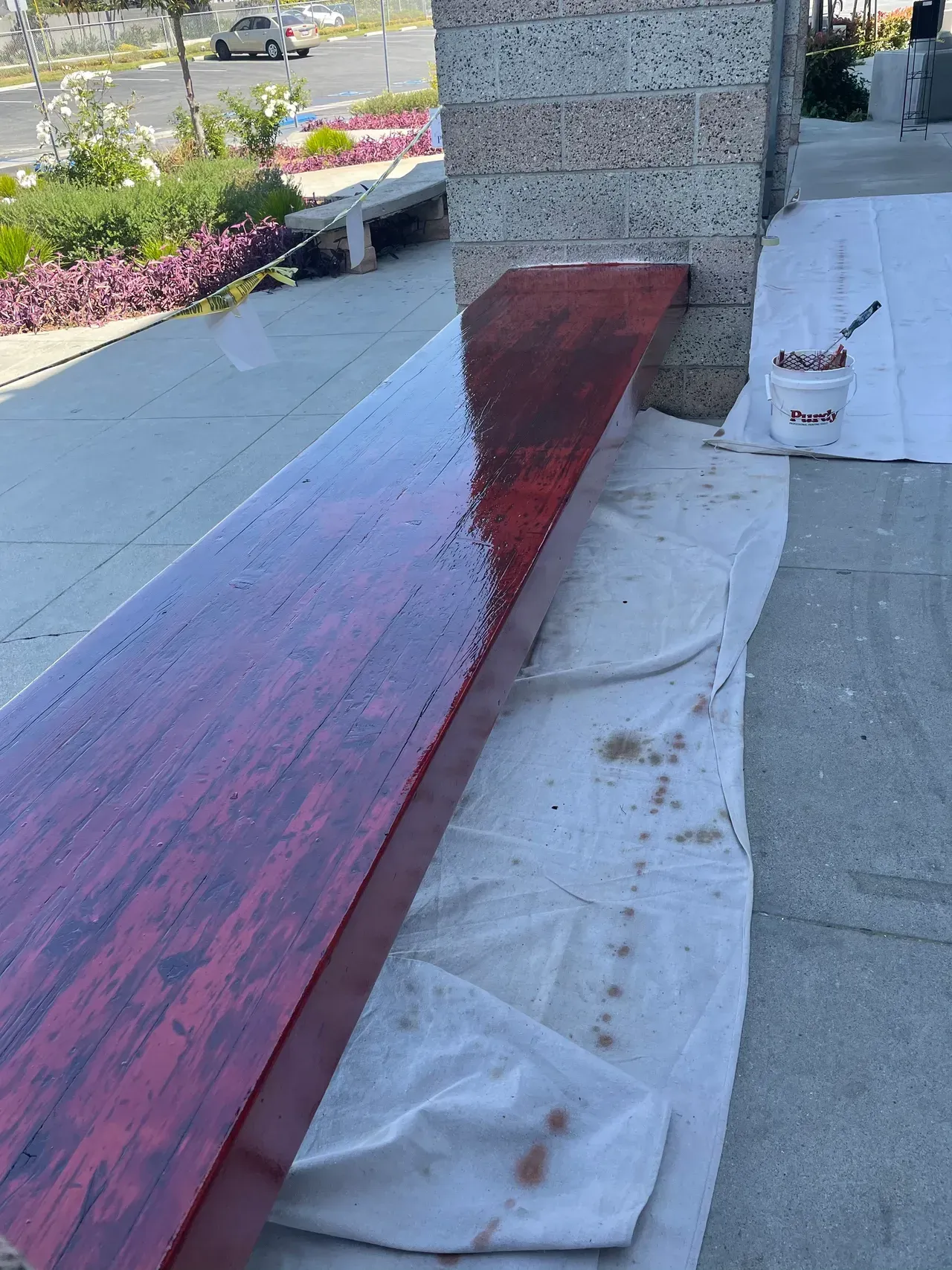 A wooden table is being painted red on a sidewalk.