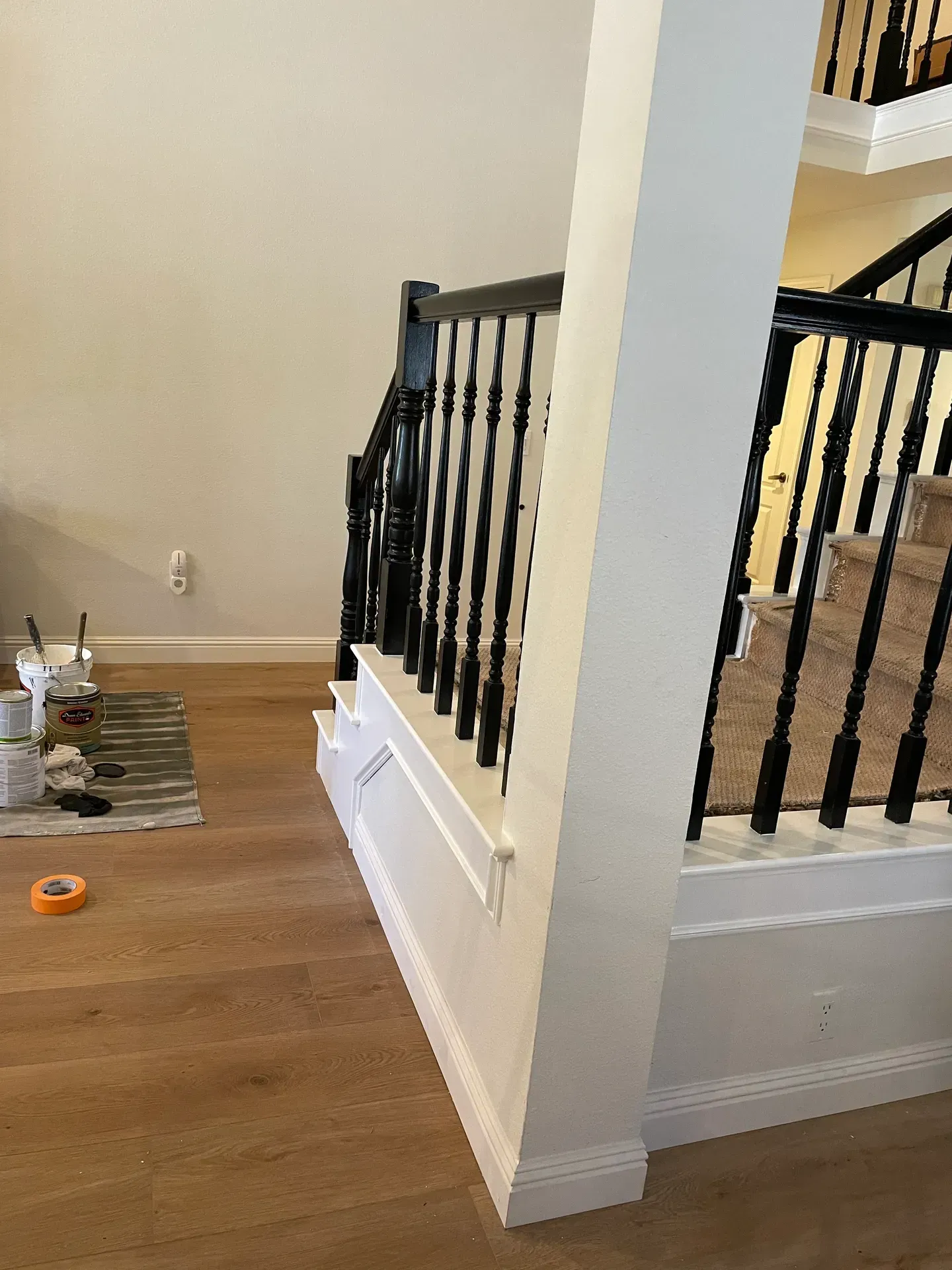 A staircase with a black railing is being painted in a living room.