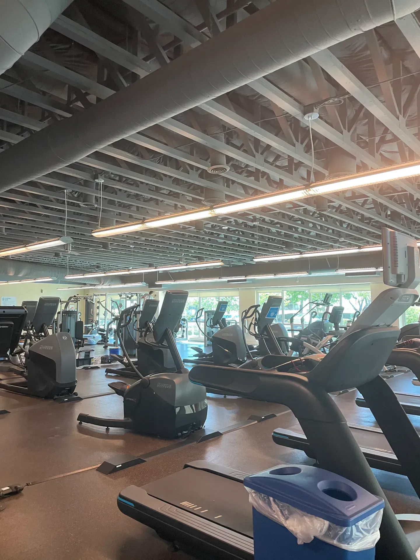 A gym filled with lots of exercise equipment and a trash can.