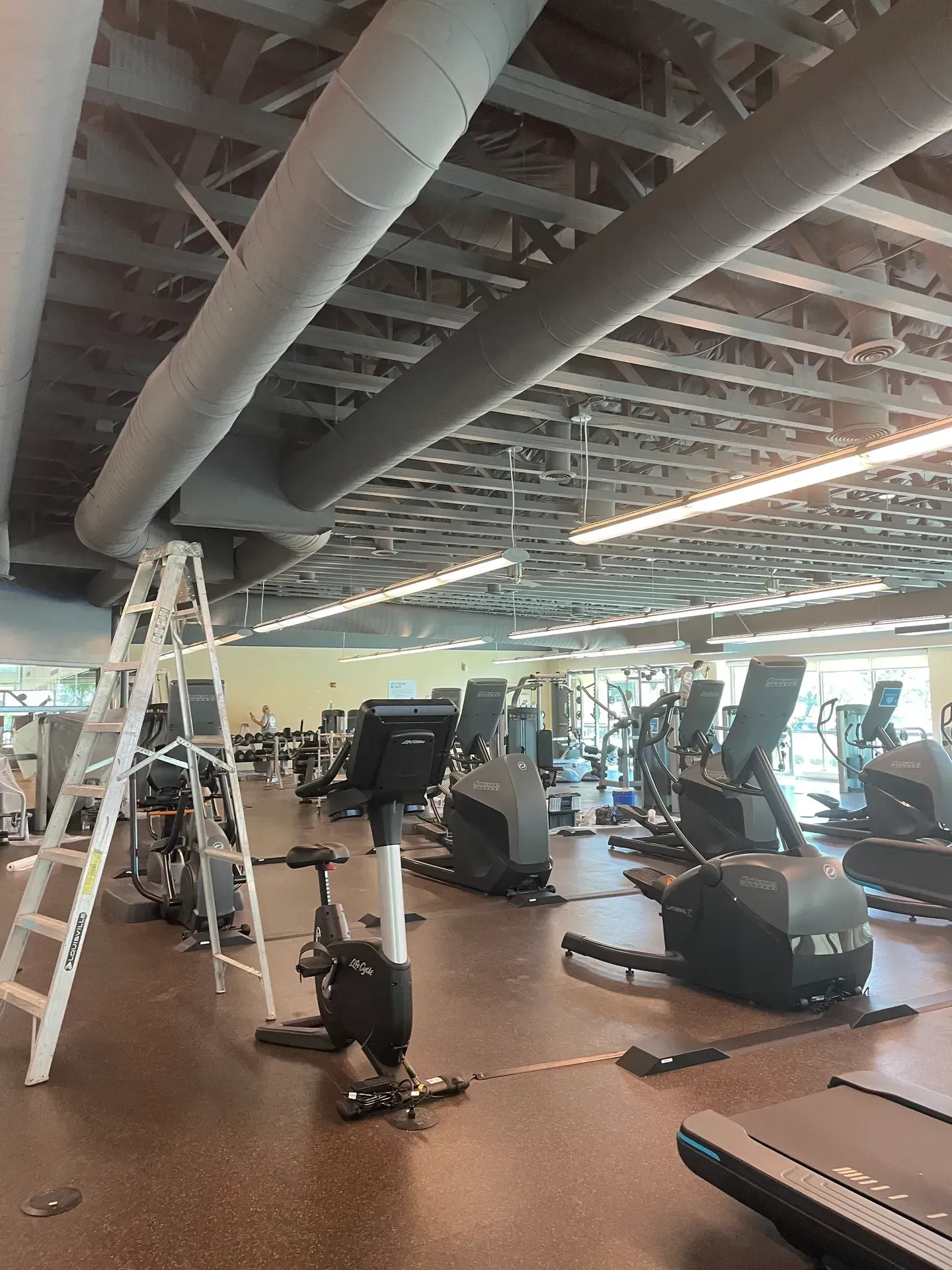 A gym with a lot of exercise equipment and a ladder.
