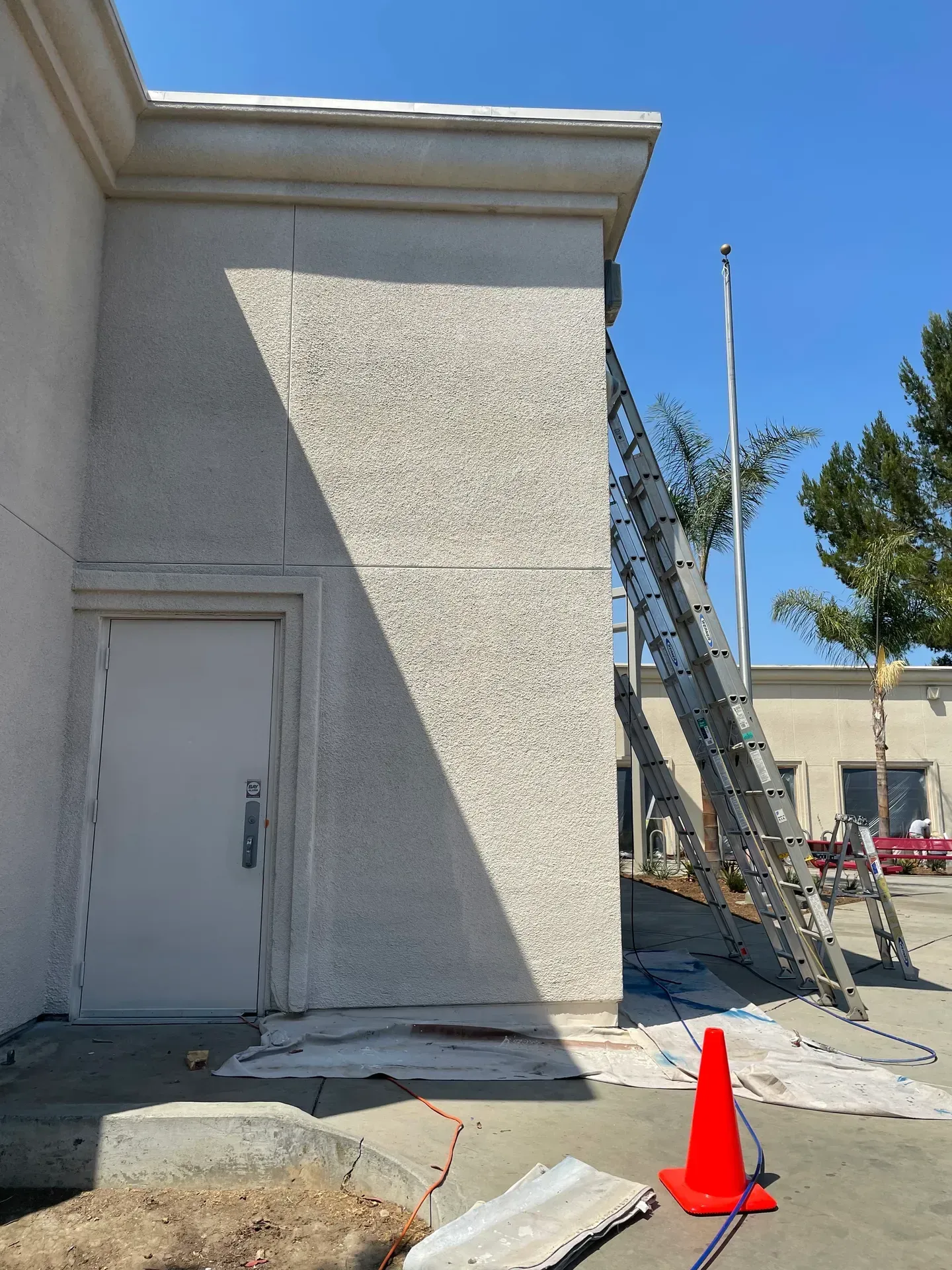 A ladder is sitting on the side of a building next to an orange cone.