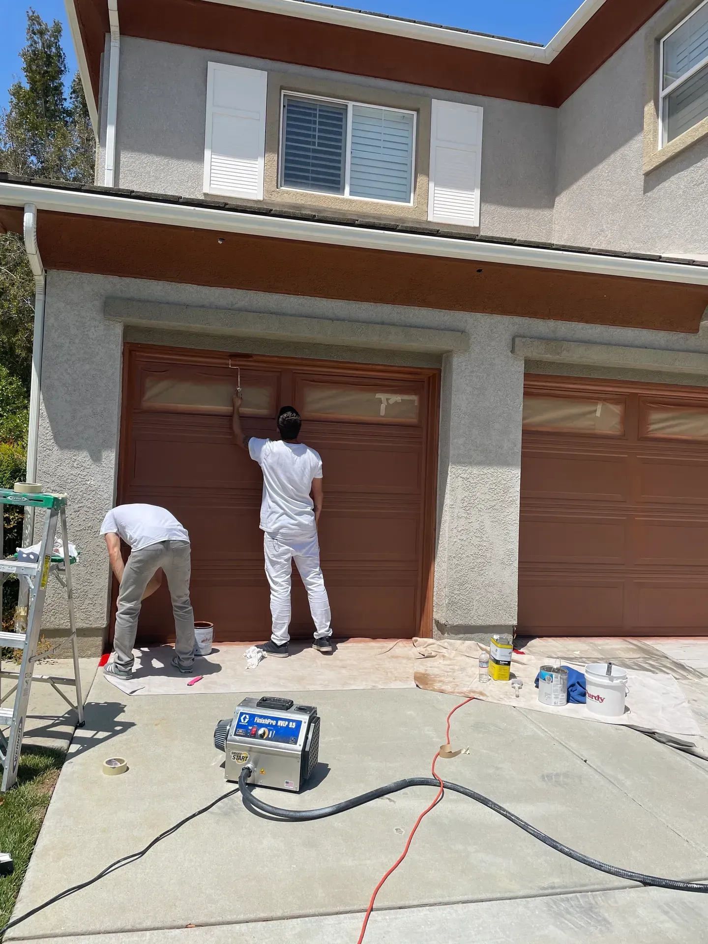 Two men are painting a garage door in front of a house.