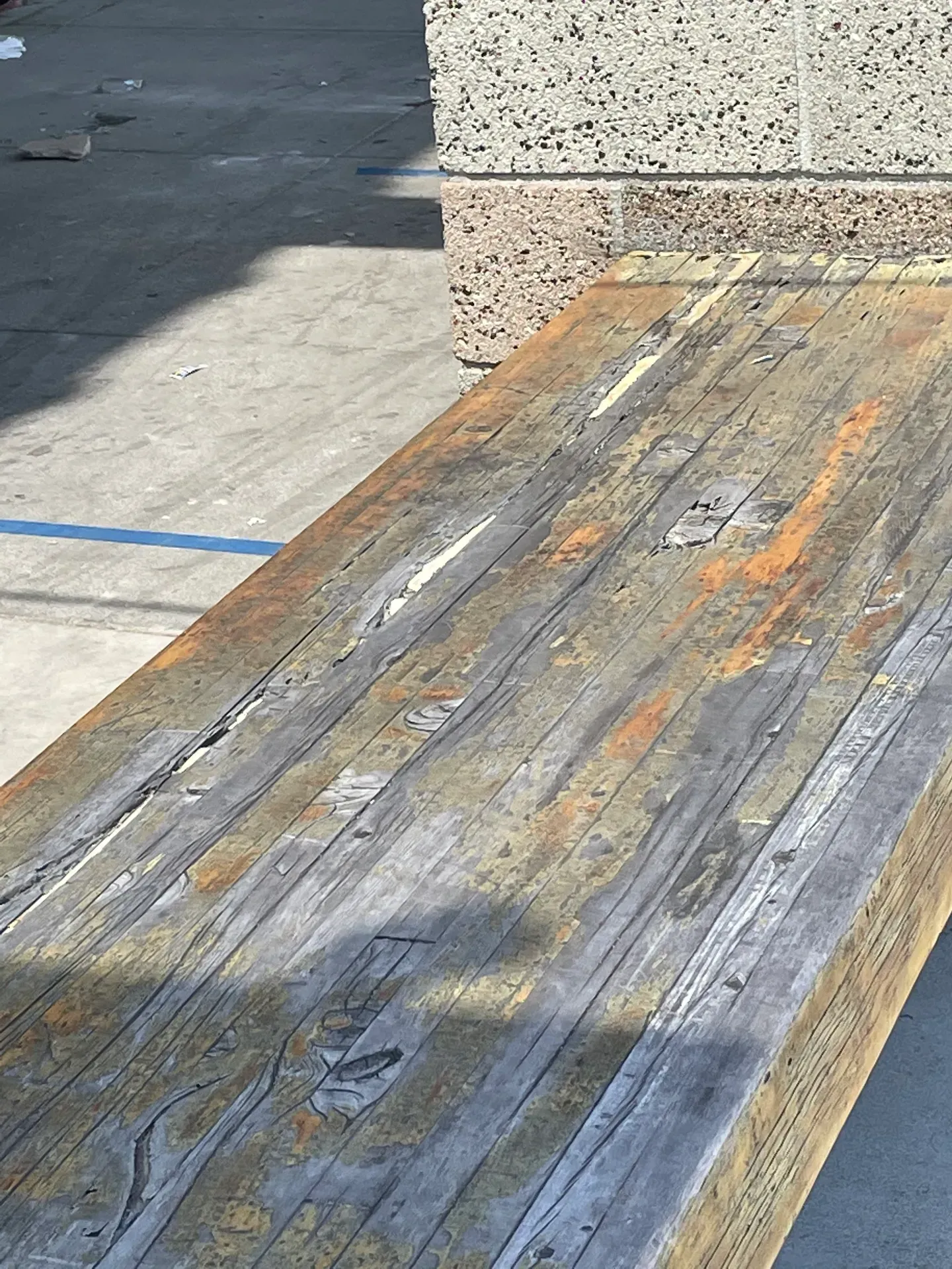 A close up of a wooden bench with a concrete wall in the background.