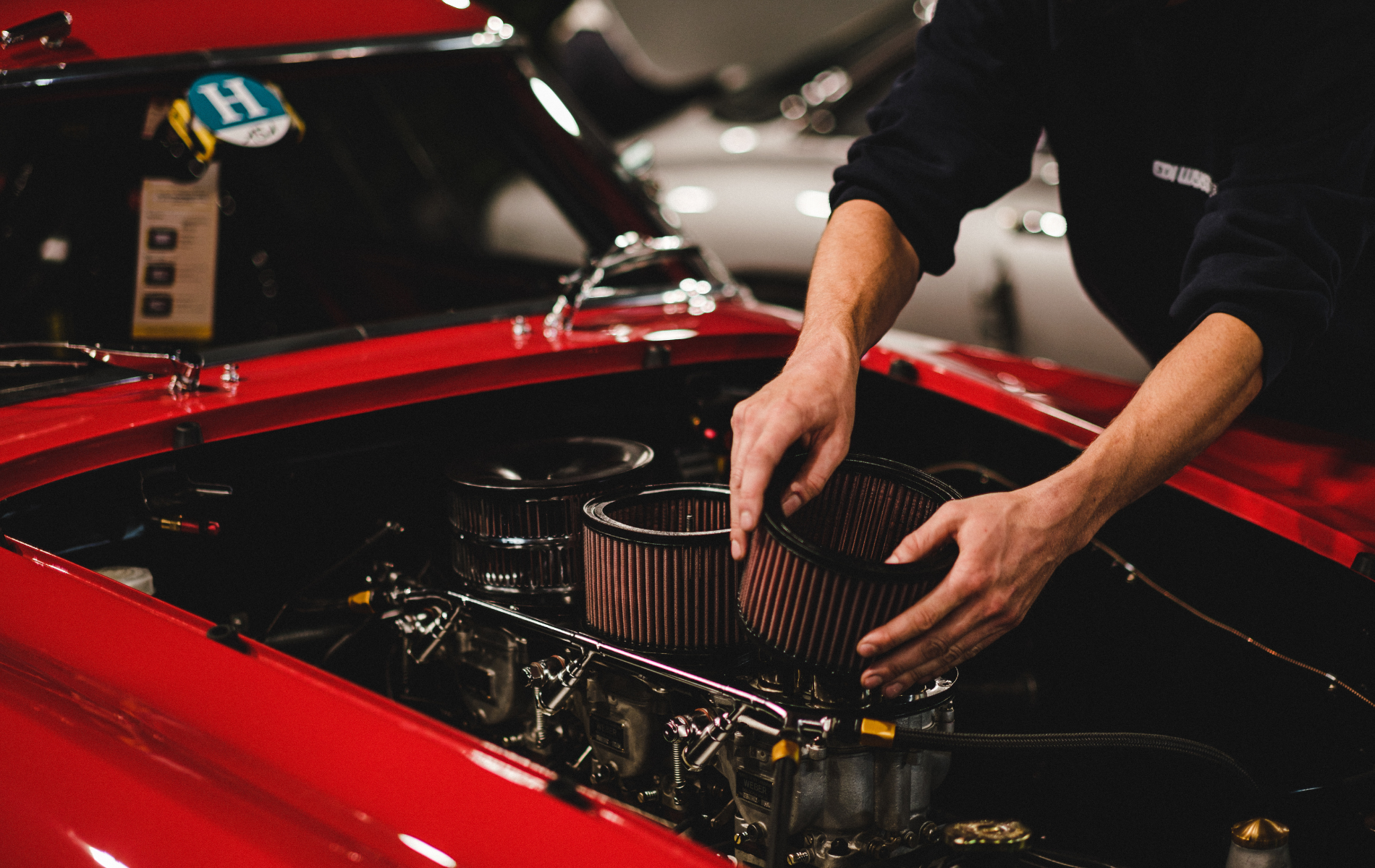 Person replacing air filter in red classic car engine bay.