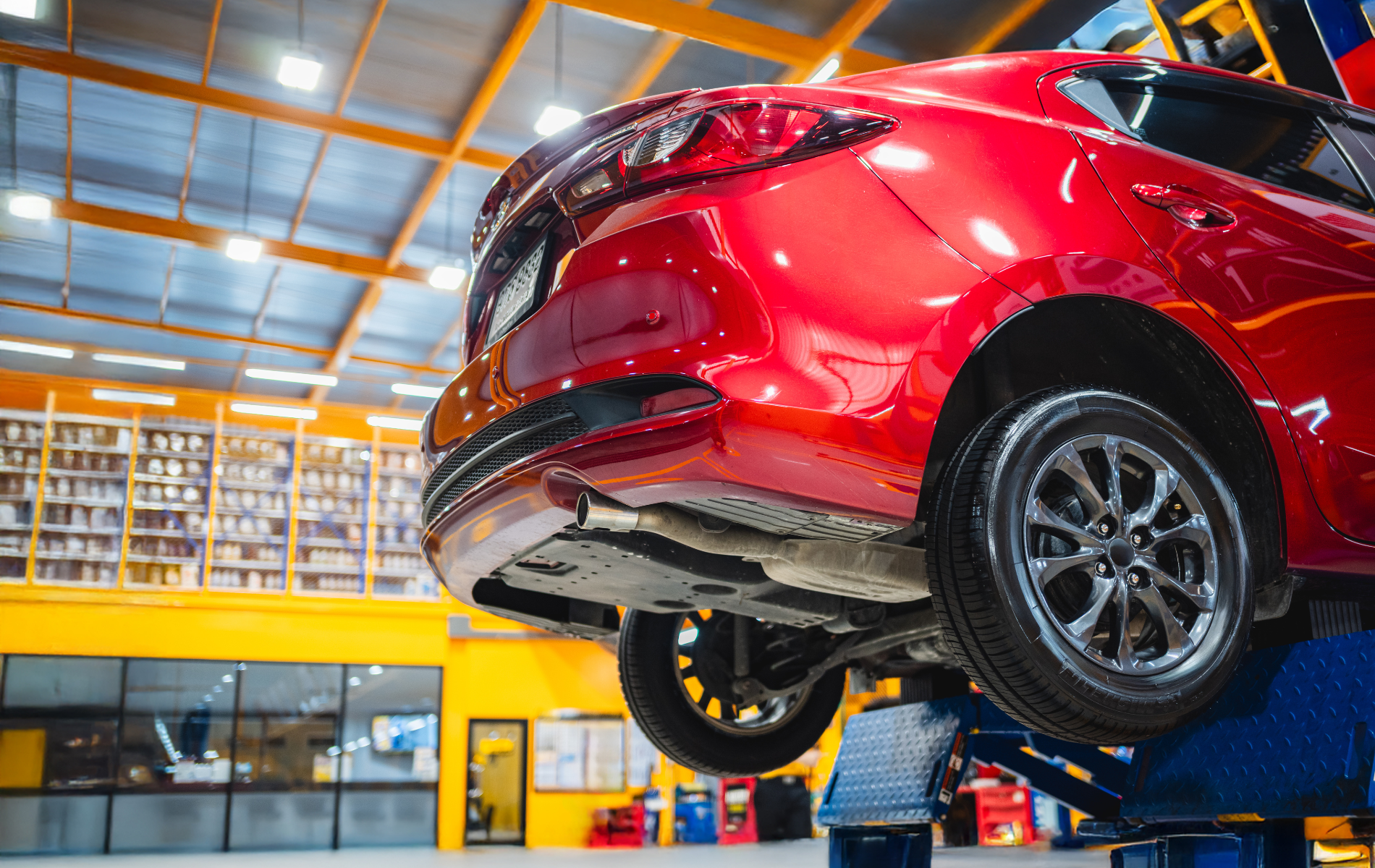 Red car raised on a lift in a brightly lit auto repair shop.