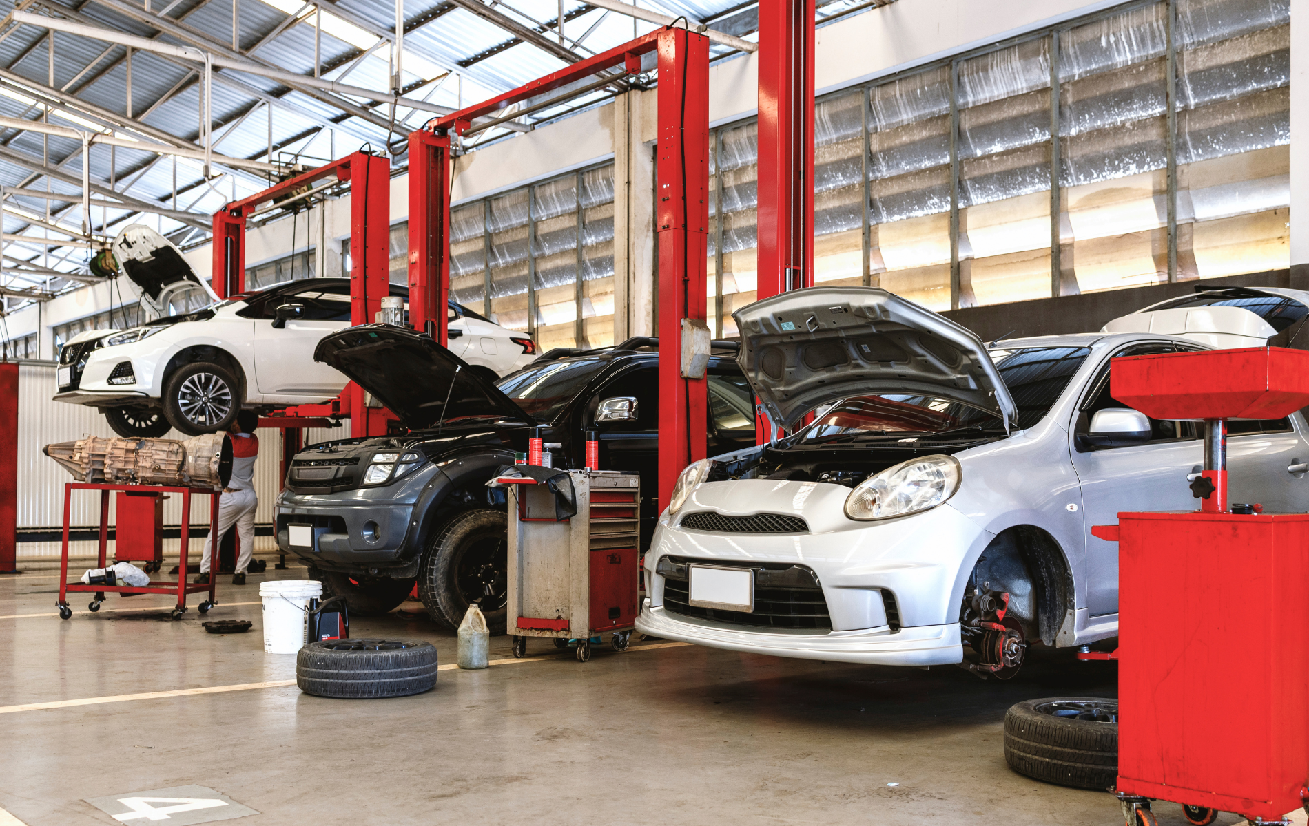 Cars in a repair shop, raised on lifts, with hoods open. Red and silver hues.