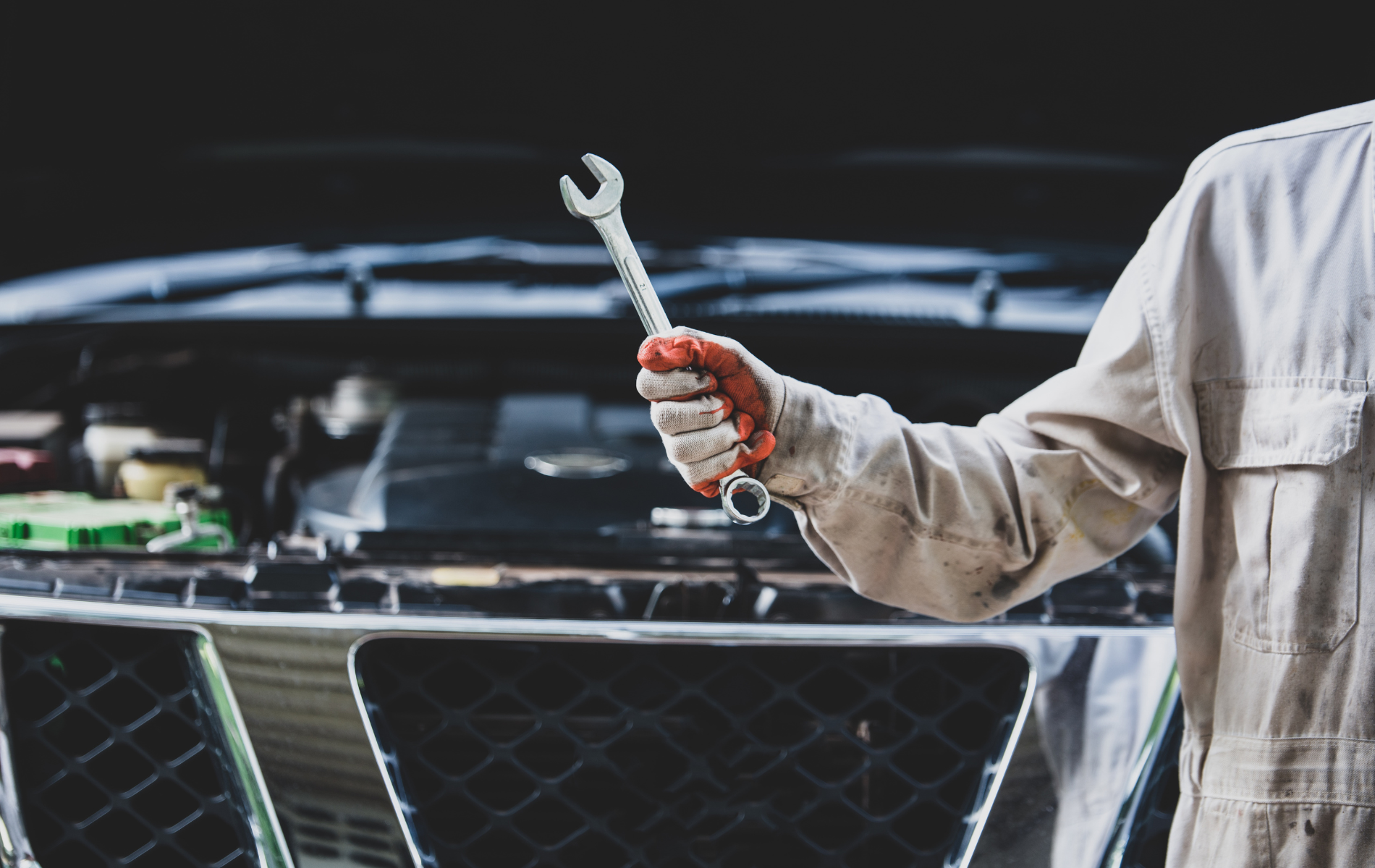 Mechanic in overalls holds a wrench, working on a car engine.