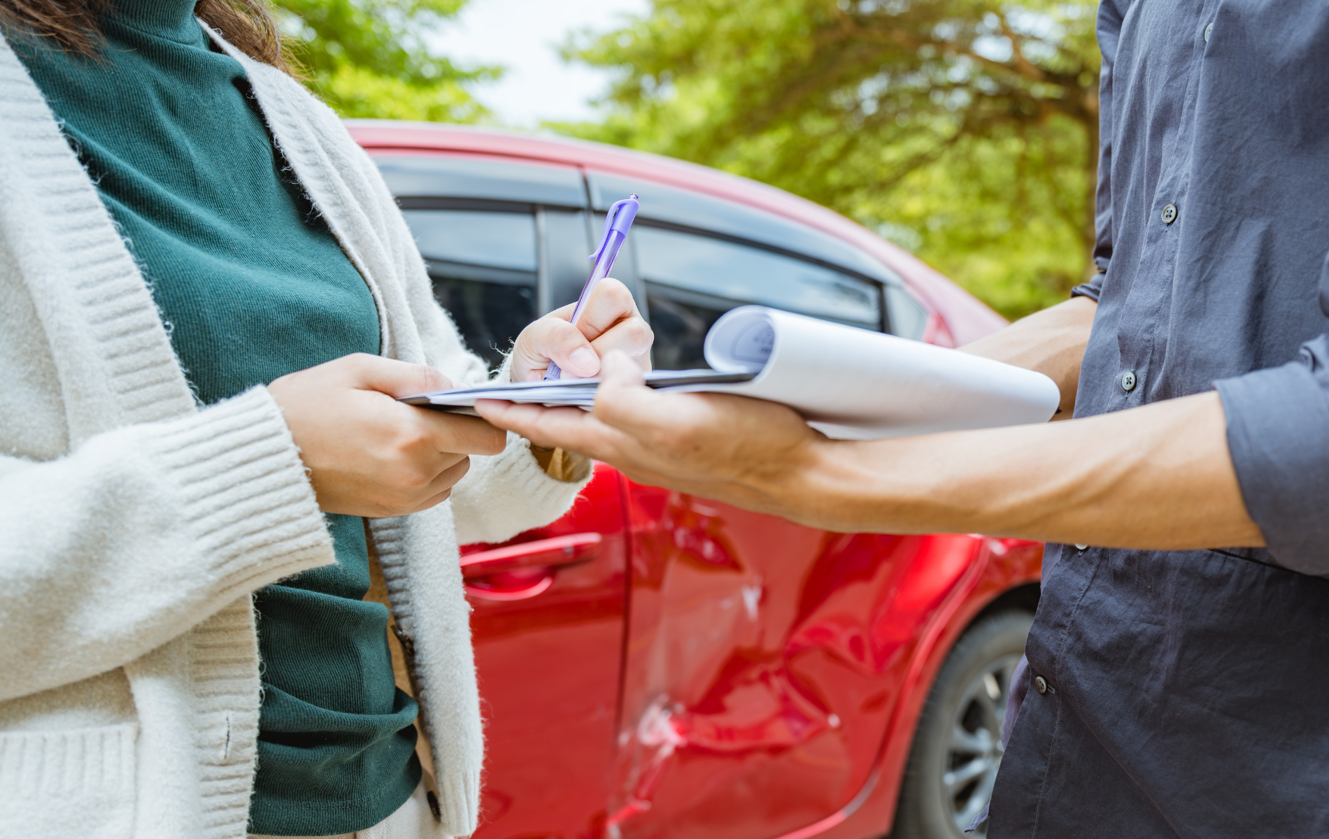 Person signing a document, red car in background.