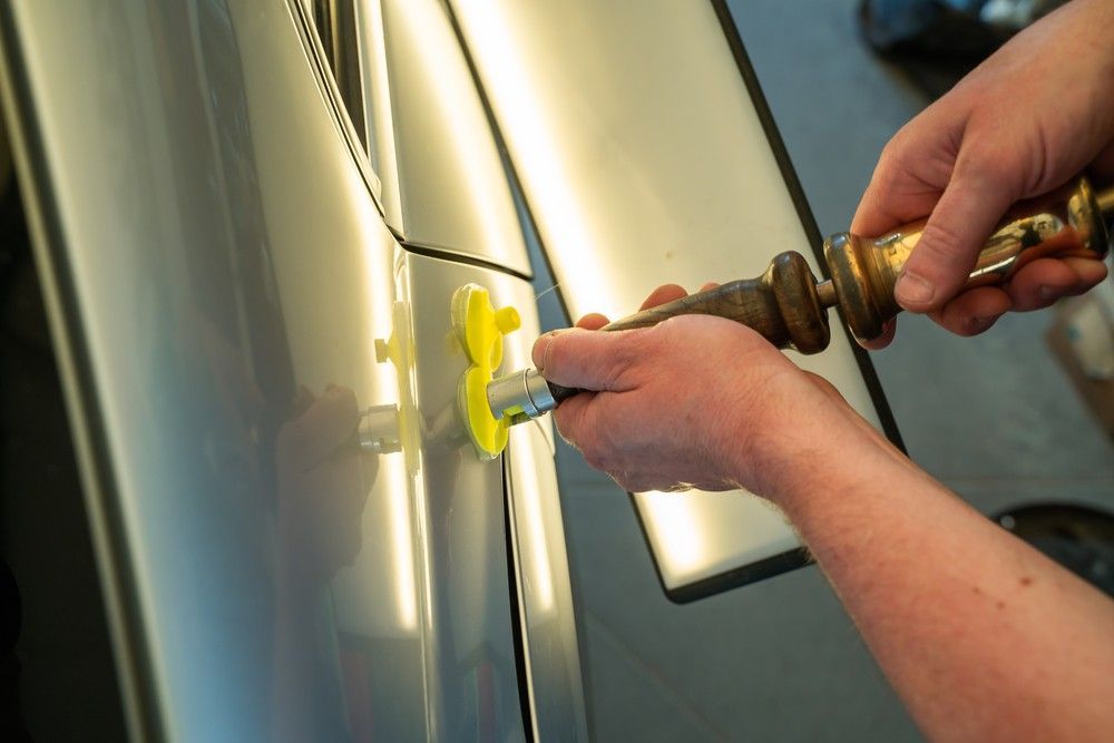 Hands using tools to remove a dent from a silver car.