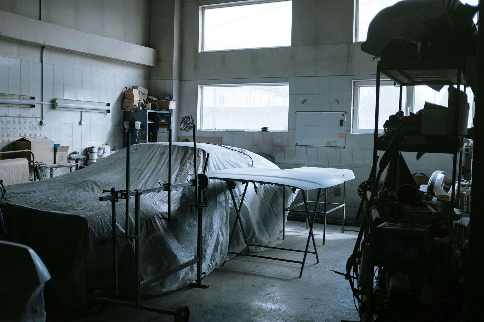 Interior of a car repair shop; car and car parts covered in white sheeting.