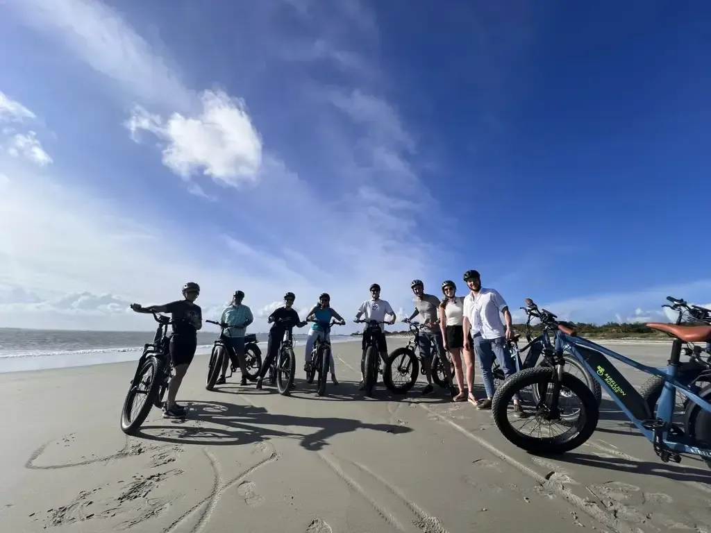 A group of people are standing on a beach with their bikes.