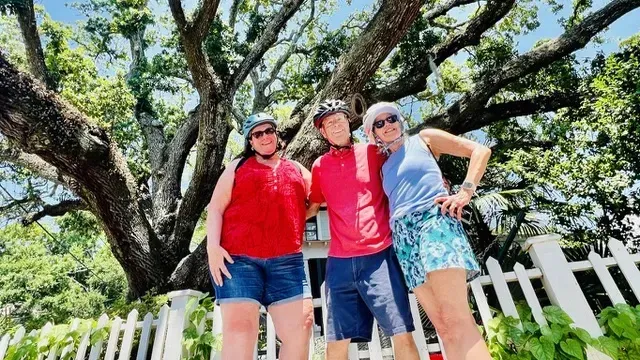 Three people are posing for a picture in front of a tree.