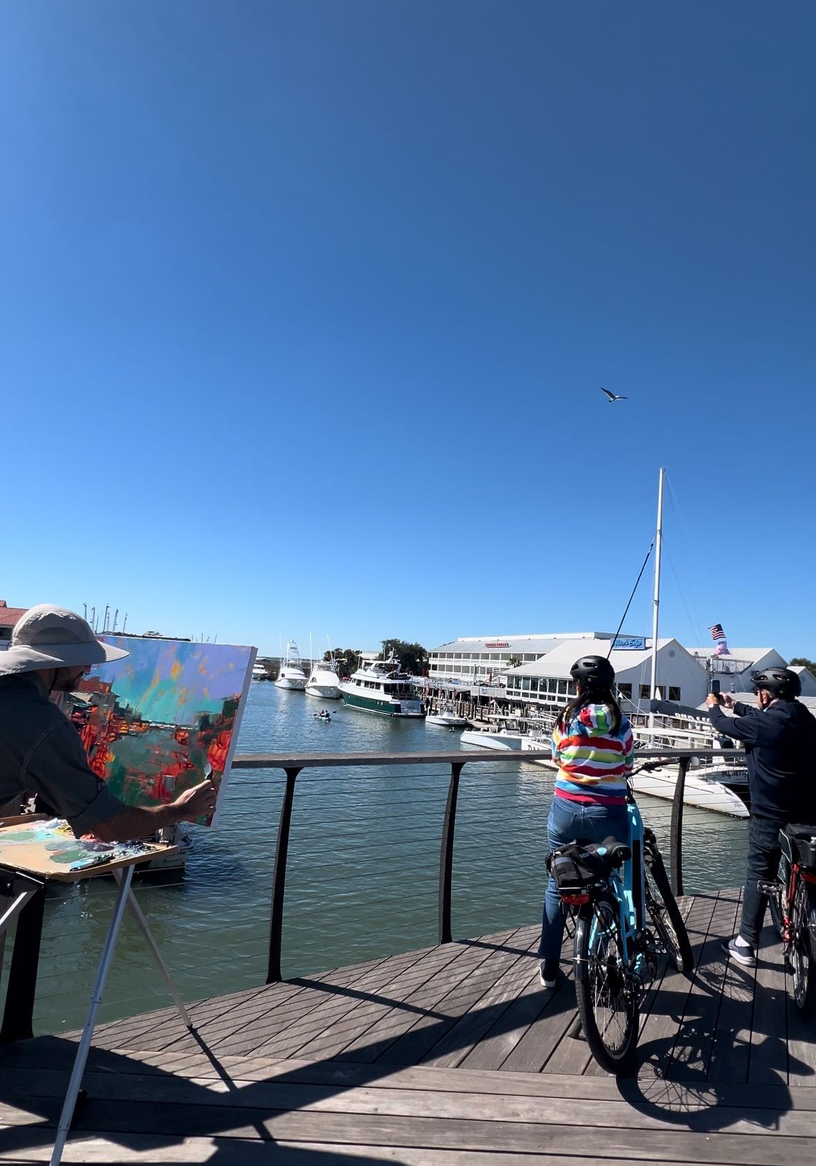a man is painting on a canvas while a woman is riding a bike on a dock .