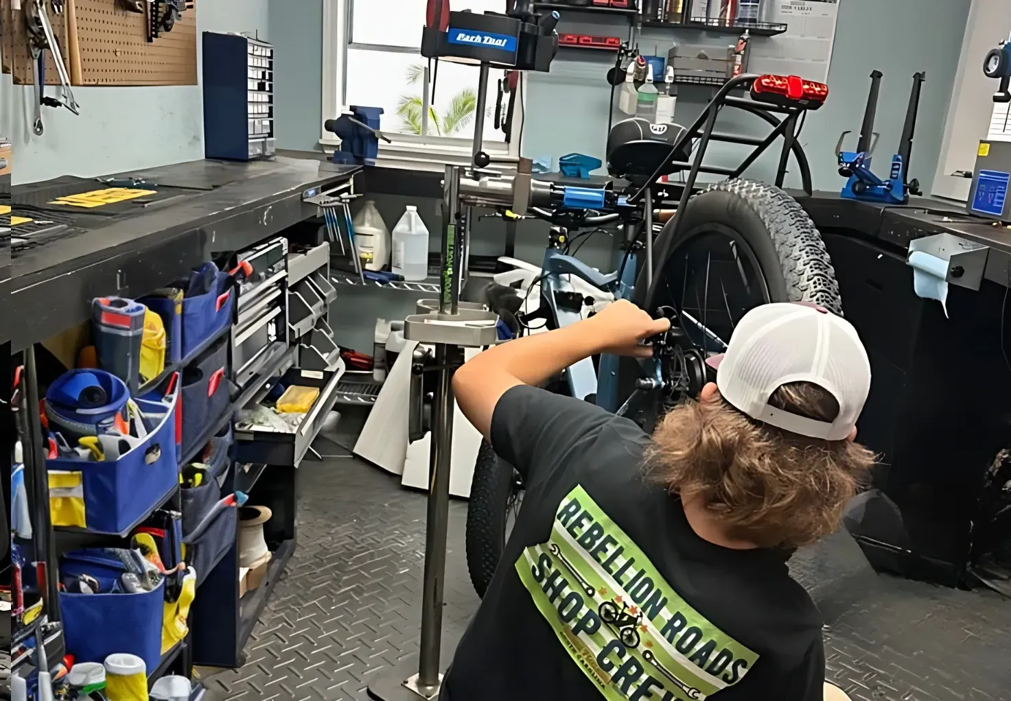 A man wearing a rebellion roads shirt is working on a bike