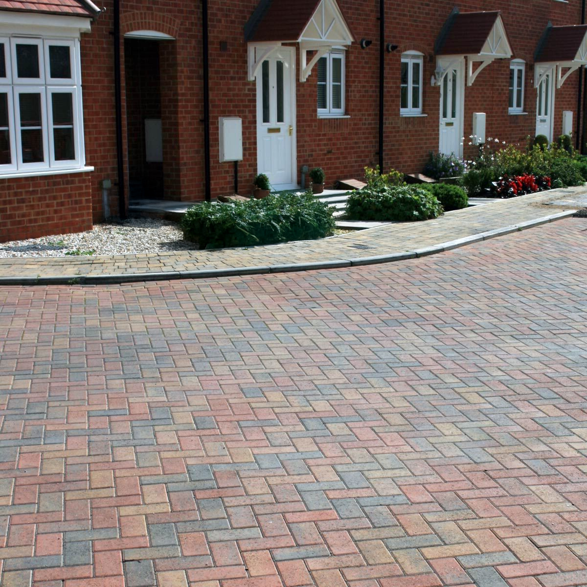 Brick paved street in front of brick houses with white doors and landscaping.