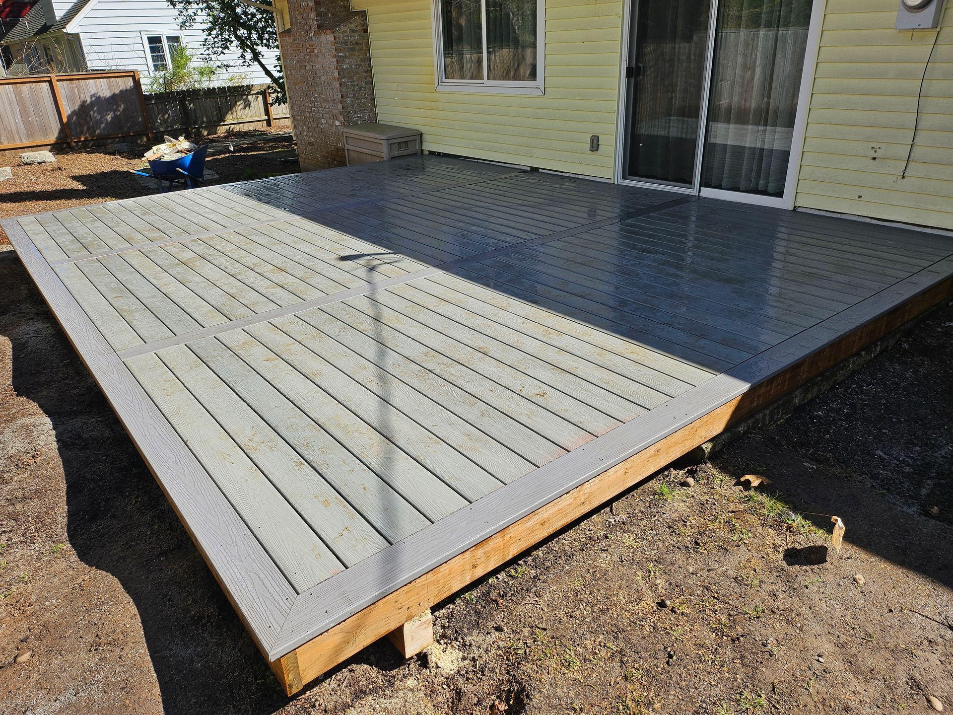 Wooden deck frame under construction outside a sliding glass door, with finished grey composite boards in the foreground.